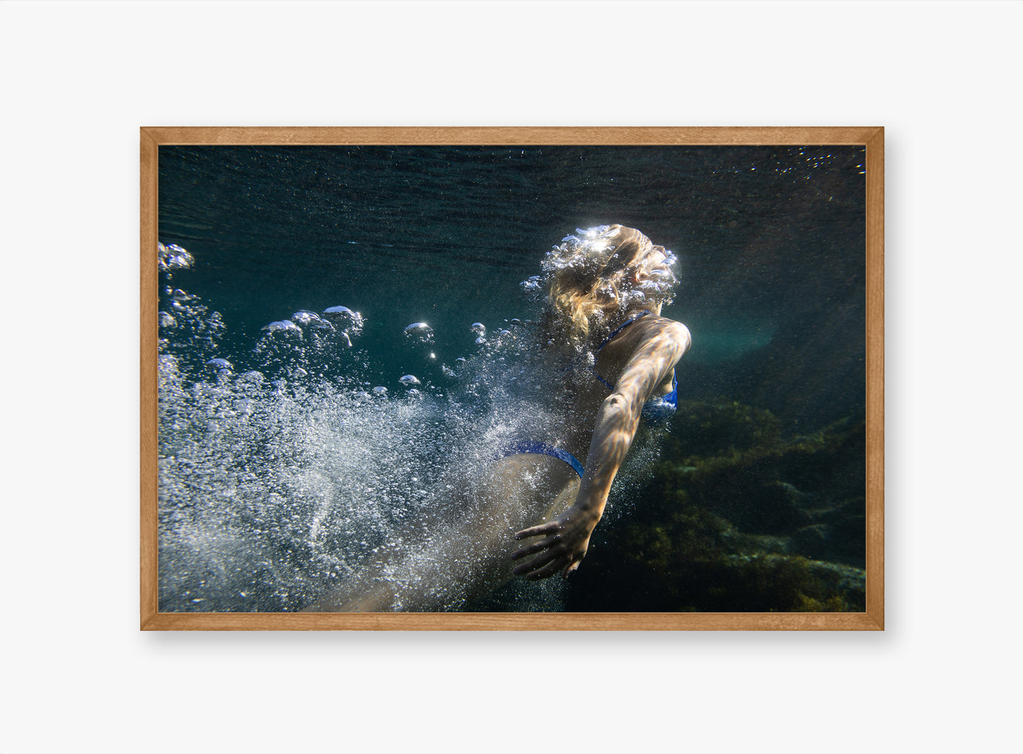 Framed artwork of a person diving underwater with bubbles, on a white wall.